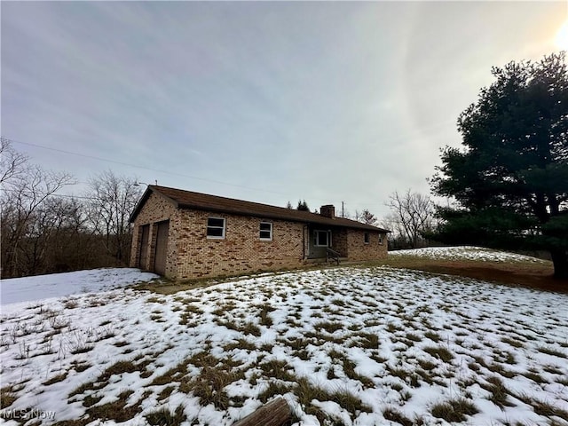 snow covered back of property featuring a garage and brick siding