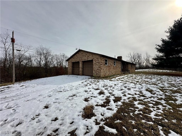 snow covered property featuring a detached garage, a chimney, and brick siding