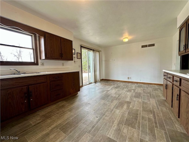 kitchen with wood finished floors, a sink, visible vents, baseboards, and light countertops