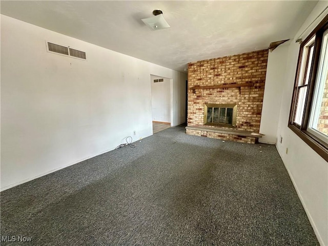 unfurnished living room featuring a brick fireplace, visible vents, and dark carpet