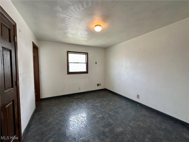 unfurnished room featuring dark floors, visible vents, and baseboards