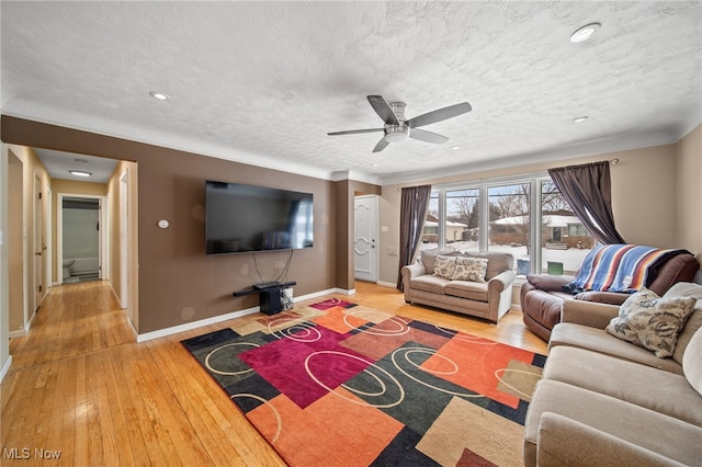 living area with a ceiling fan, ornamental molding, a textured ceiling, wood finished floors, and baseboards