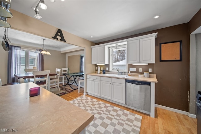 kitchen featuring white cabinets, decorative light fixtures, light countertops, stainless steel dishwasher, and a sink