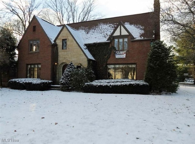 english style home with stone siding, brick siding, a chimney, and roof with shingles