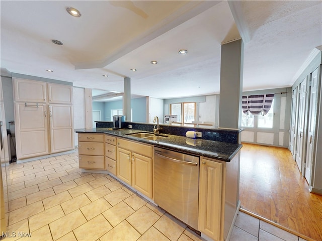 kitchen with dark stone counters, light brown cabinets, a sink, and stainless steel dishwasher