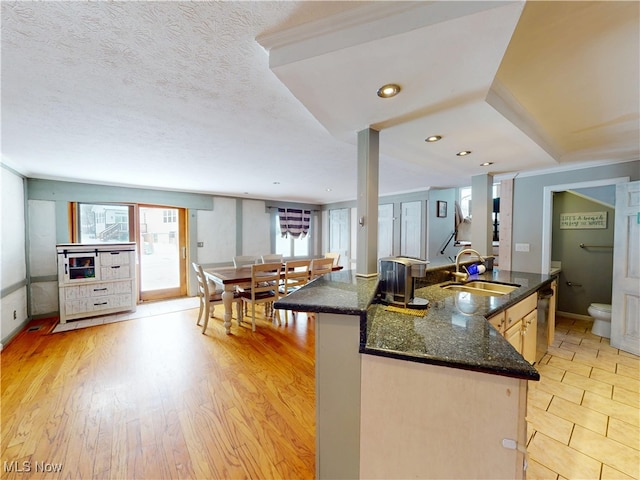 kitchen with light wood finished floors, dishwasher, an island with sink, open floor plan, and a sink