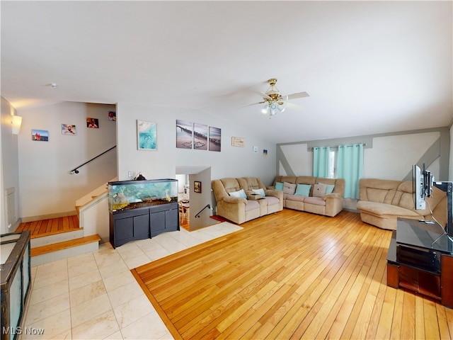 living room featuring lofted ceiling, ceiling fan, stairway, and light wood-style flooring