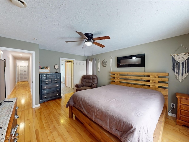 bedroom with a ceiling fan, baseboards, light wood-style flooring, and a textured ceiling