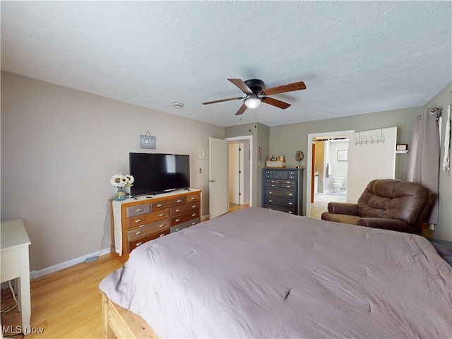 bedroom featuring a textured ceiling, ceiling fan, baseboards, light wood-type flooring, and ensuite bath