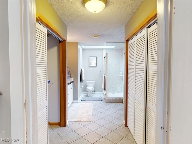 hallway with light tile patterned flooring, a textured ceiling, and baseboards