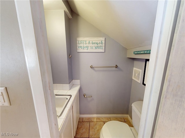 half bathroom with lofted ceiling, toilet, vanity, baseboards, and tile patterned floors