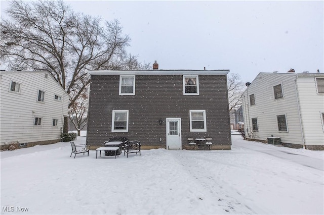 snow covered house with a chimney and central AC unit