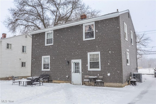 snow covered property featuring central air condition unit and a chimney