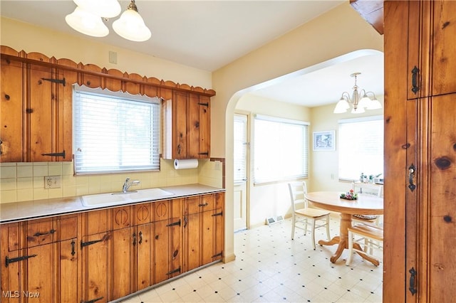 kitchen featuring decorative light fixtures, light floors, light countertops, brown cabinetry, and a sink