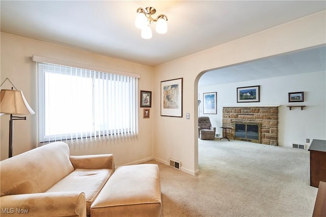 living area featuring light colored carpet, visible vents, a fireplace, and arched walkways