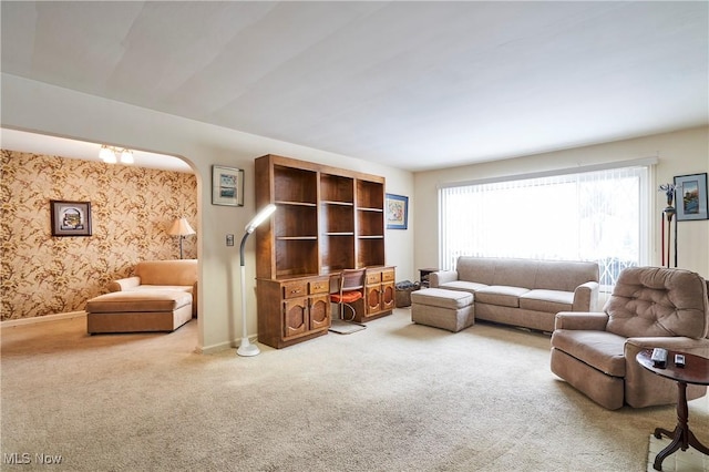 carpeted living room with wallpapered walls, baseboards, and arched walkways