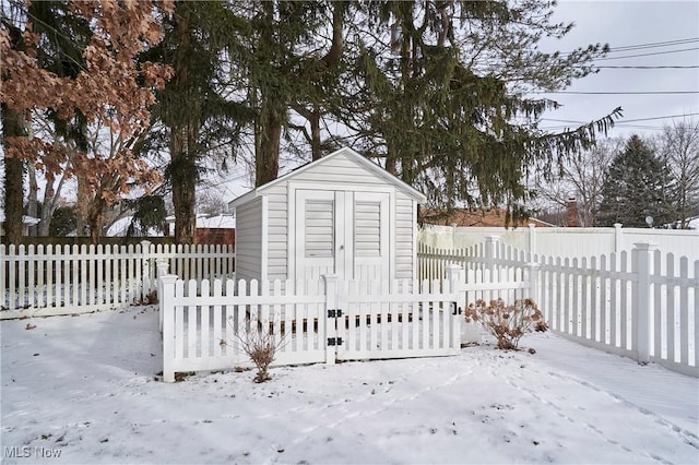 snow covered structure with a fenced backyard, an outdoor structure, and a shed