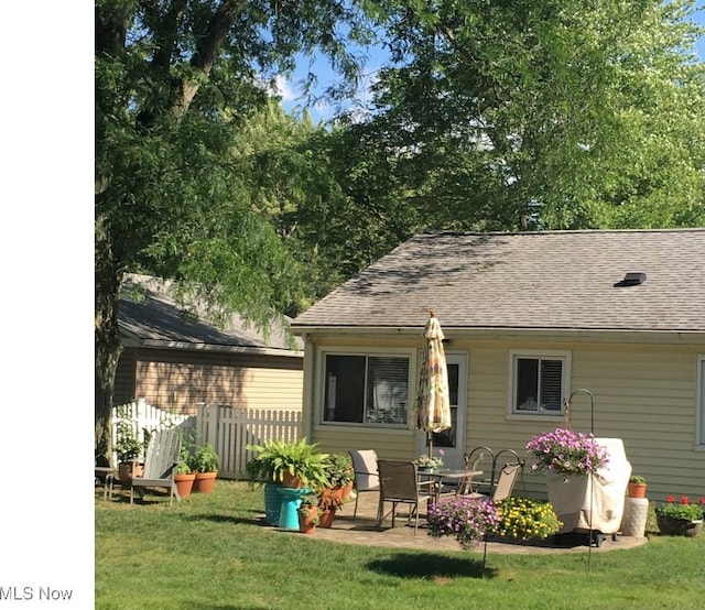 rear view of property with roof with shingles, a lawn, a patio, and fence