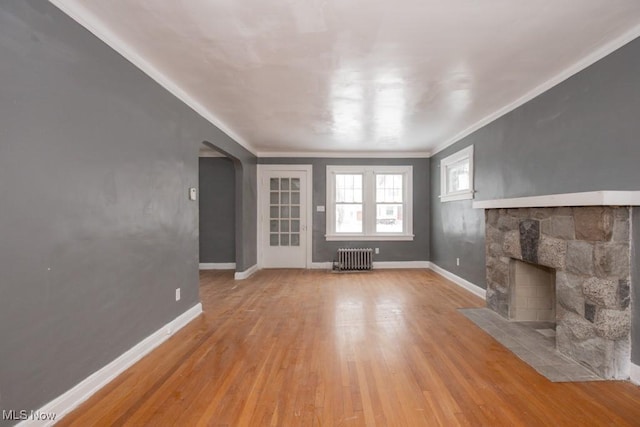 unfurnished living room featuring arched walkways, a fireplace, radiator heating unit, light wood-type flooring, and baseboards