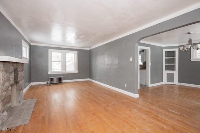 unfurnished living room with radiator, light wood finished floors, arched walkways, and a stone fireplace