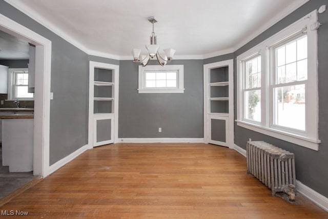 unfurnished dining area featuring radiator, baseboards, built in features, and a wealth of natural light