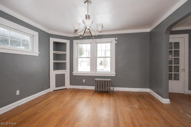 unfurnished dining area featuring arched walkways, radiator, baseboards, and wood finished floors