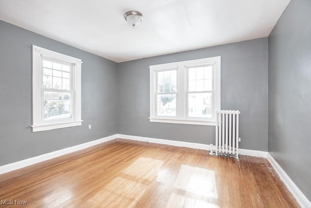 empty room featuring light wood-type flooring, radiator heating unit, and baseboards