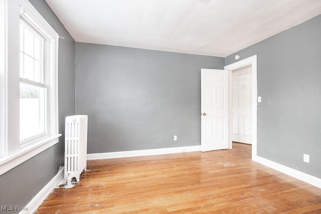 unfurnished room featuring light wood-style floors, radiator, and baseboards