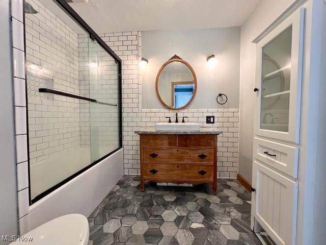 full bathroom featuring enclosed tub / shower combo, toilet, tile walls, and vanity