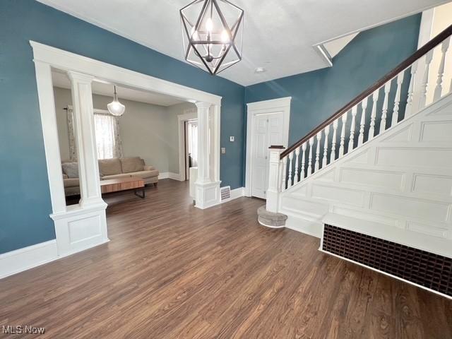 entrance foyer featuring visible vents, baseboards, stairs, dark wood finished floors, and decorative columns