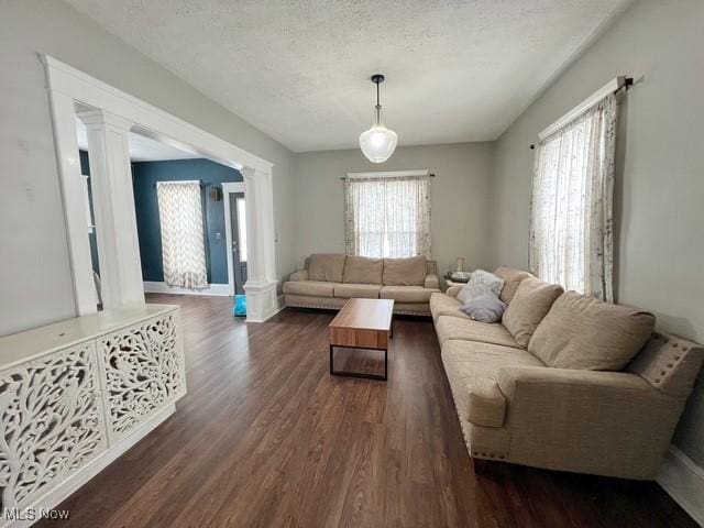 living room featuring dark wood-style floors, a textured ceiling, plenty of natural light, and decorative columns