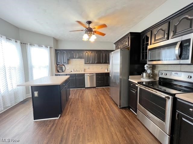 kitchen featuring dark wood-style floors, stainless steel appliances, light countertops, decorative backsplash, and a kitchen island