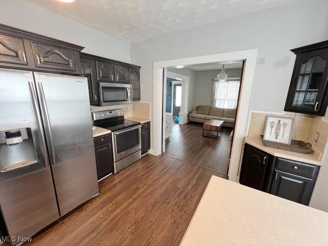 kitchen featuring dark wood-type flooring, light countertops, appliances with stainless steel finishes, tasteful backsplash, and glass insert cabinets