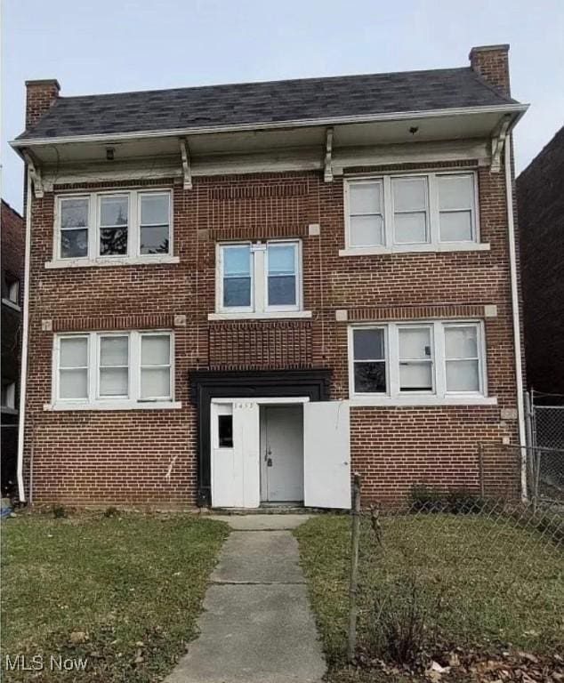 view of front of house featuring brick siding, fence, a chimney, and a front lawn