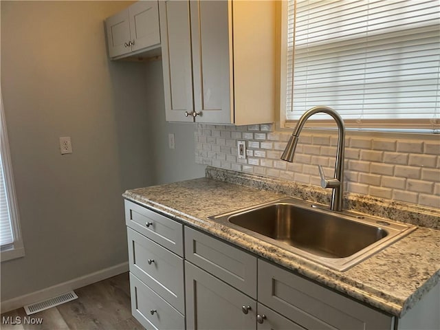 kitchen with dark wood finished floors, tasteful backsplash, gray cabinets, visible vents, and a sink