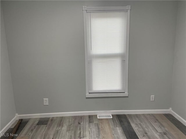 unfurnished room with a wealth of natural light, visible vents, baseboards, and wood finished floors