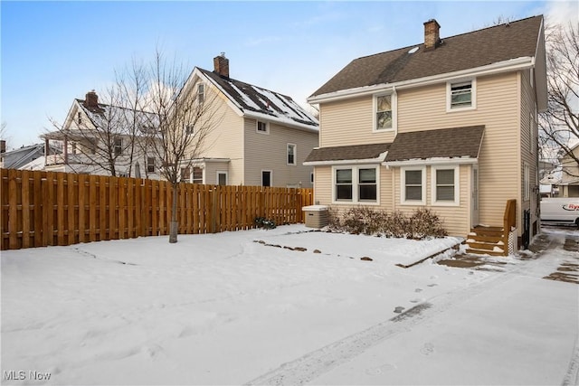 snow covered property featuring a shingled roof and fence