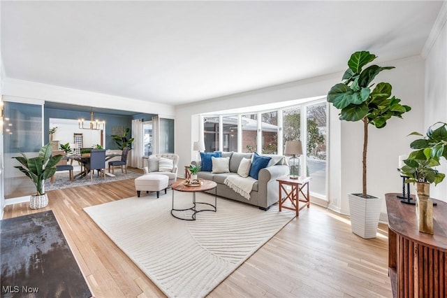 living area with light wood finished floors, ornamental molding, and a notable chandelier