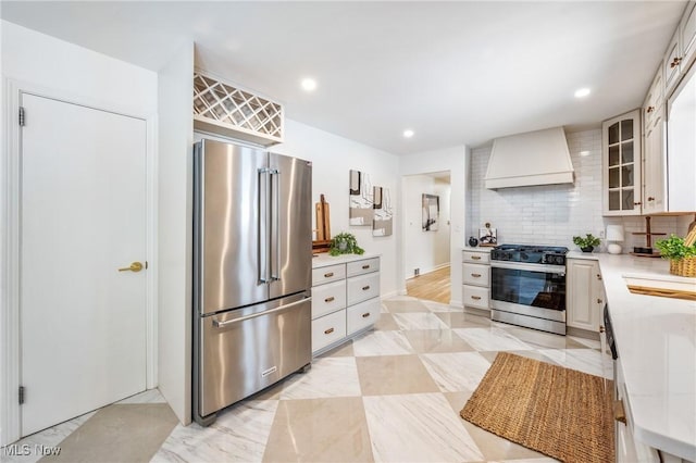 kitchen with stainless steel appliances, light countertops, glass insert cabinets, white cabinets, and wall chimney range hood