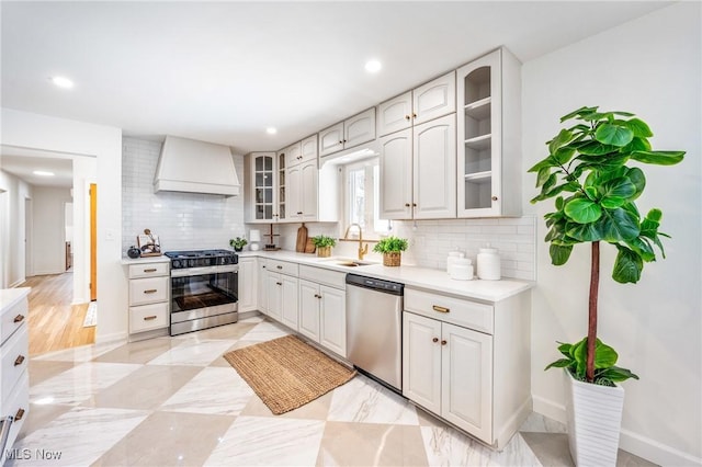 kitchen with white cabinets, glass insert cabinets, appliances with stainless steel finishes, custom exhaust hood, and light countertops