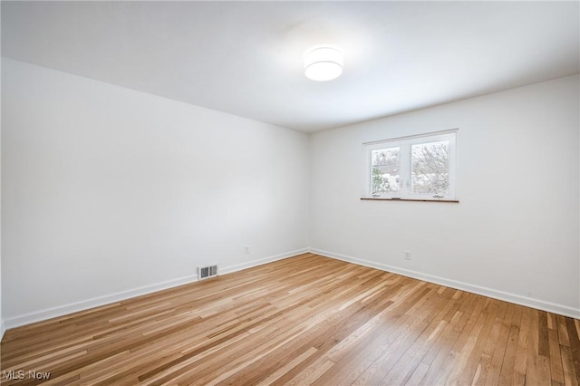 empty room with light wood-style floors, visible vents, and baseboards