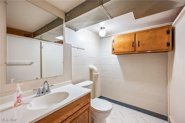 bathroom featuring toilet, marble finish floor, vanity, and concrete block wall