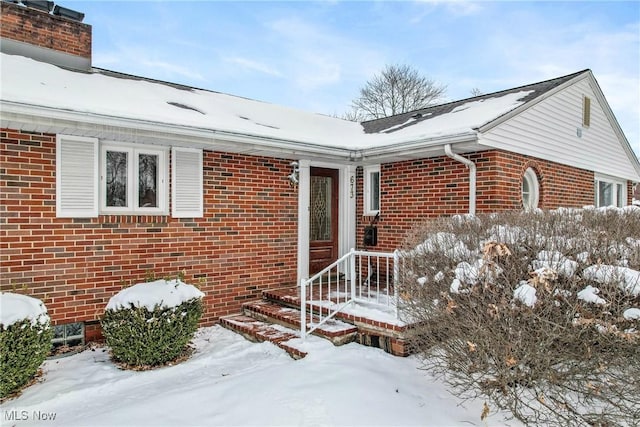 snow covered property entrance featuring brick siding