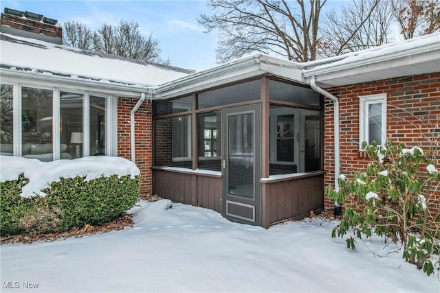 view of snow covered exterior featuring a sunroom and brick siding