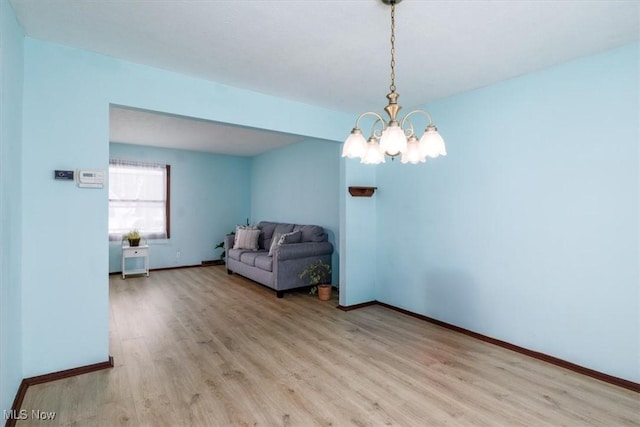 unfurnished room with baseboards, an inviting chandelier, and light wood-style floors