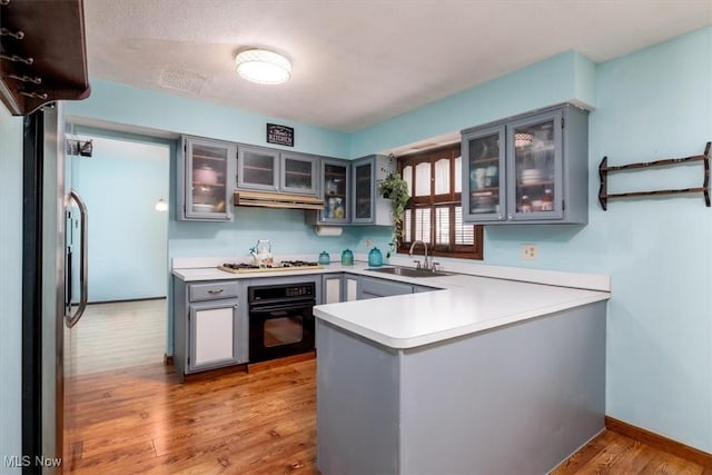 kitchen with glass insert cabinets, light countertops, a sink, and black oven