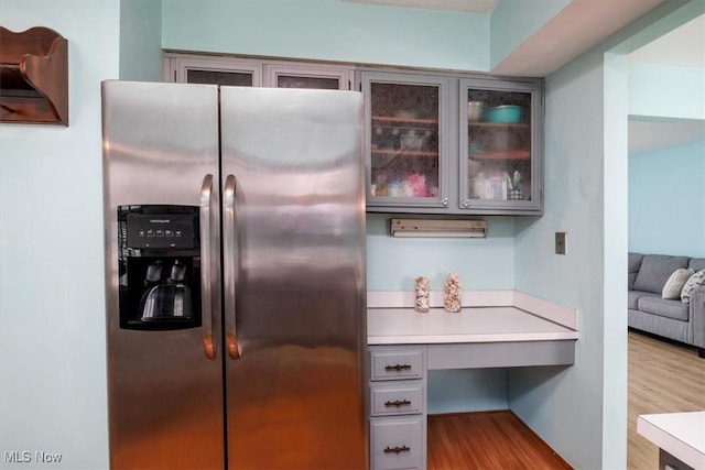 kitchen with gray cabinets, light countertops, glass insert cabinets, light wood-type flooring, and stainless steel fridge with ice dispenser