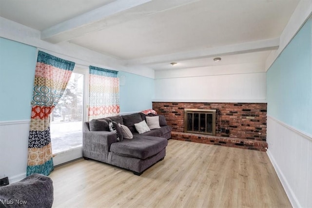 living area featuring a wainscoted wall, a brick fireplace, wood finished floors, and beam ceiling