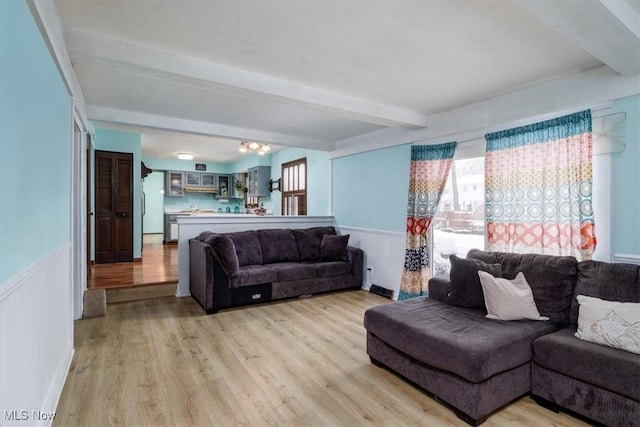 living area featuring wainscoting, beamed ceiling, and light wood finished floors