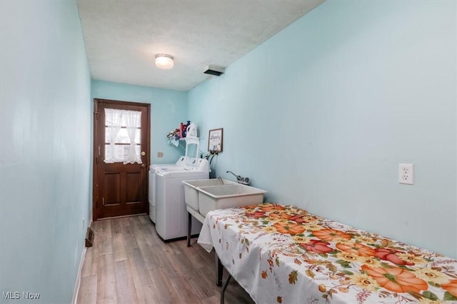 clothes washing area with laundry area, a sink, light wood-style flooring, and washer and clothes dryer